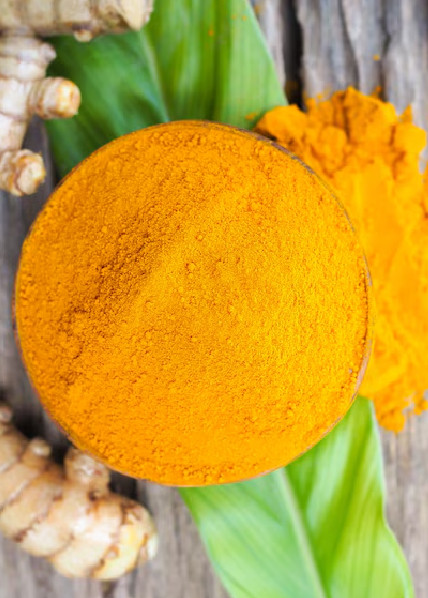 Turmeric powder in a bowl with roots and green leaf